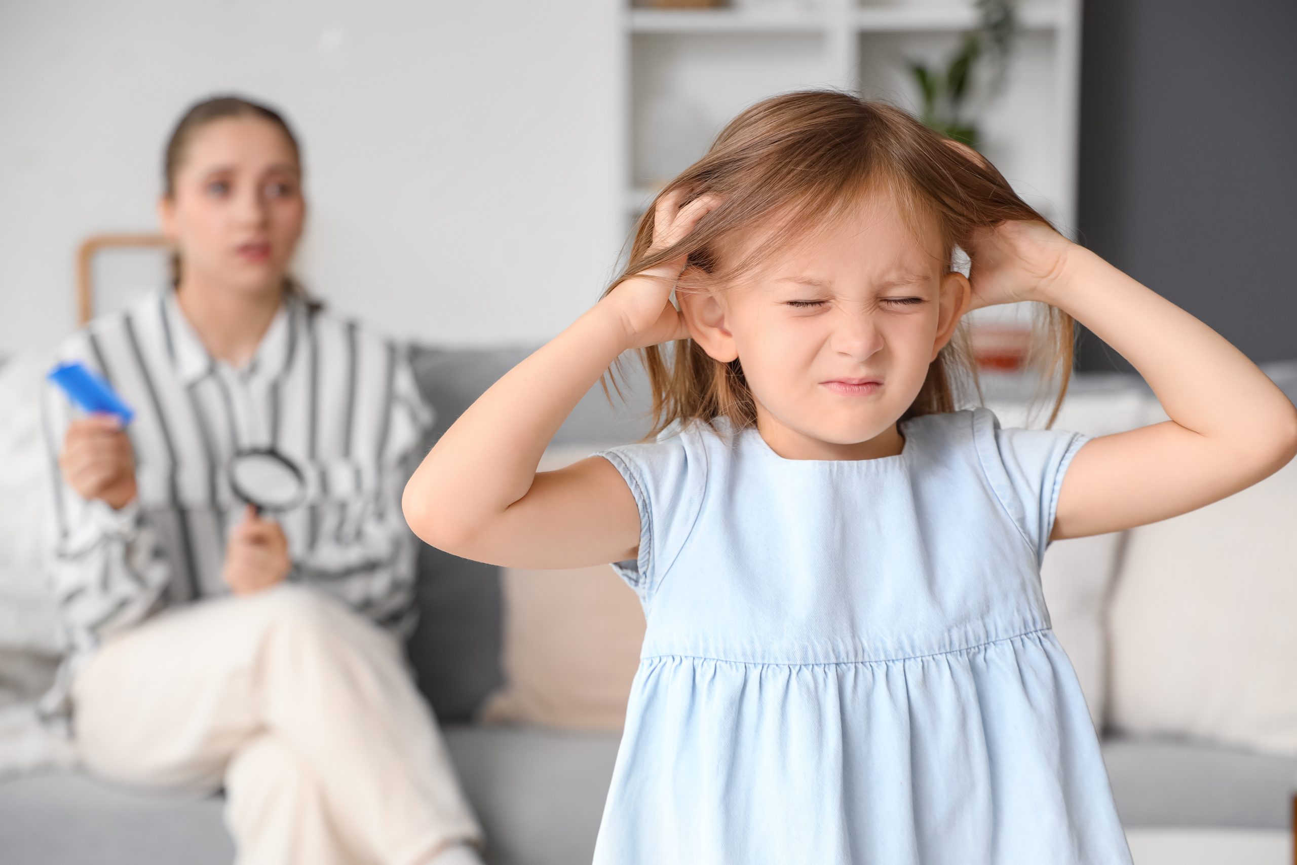 Child scratching an itchy scalp while a parent prepares to check for head lice
