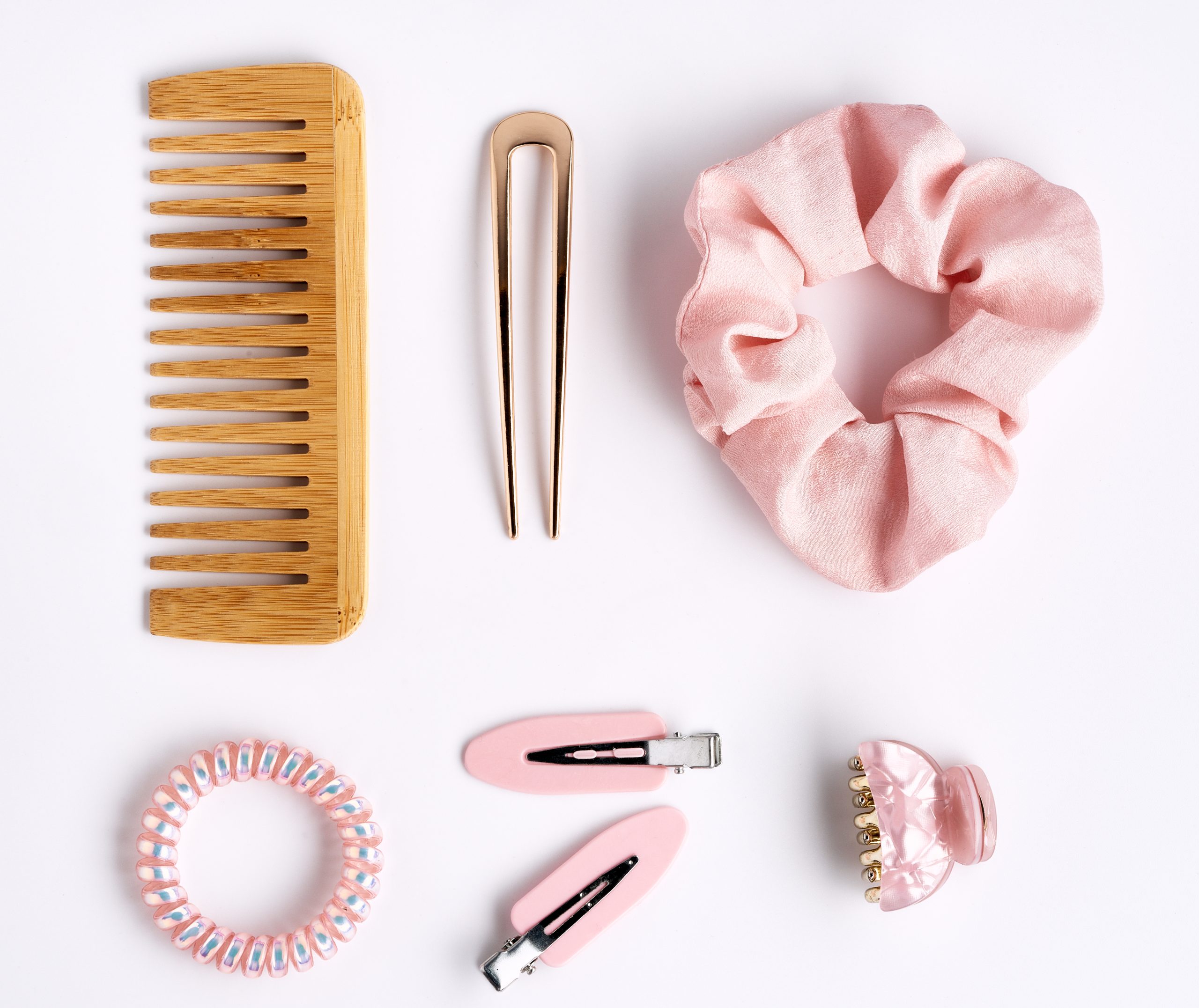 Flat-lay of children's hair accessories on a white background — fabric scrunchies, hair clips, a headband, and a small hairbrush — illustrating which items to clean after a lice case.