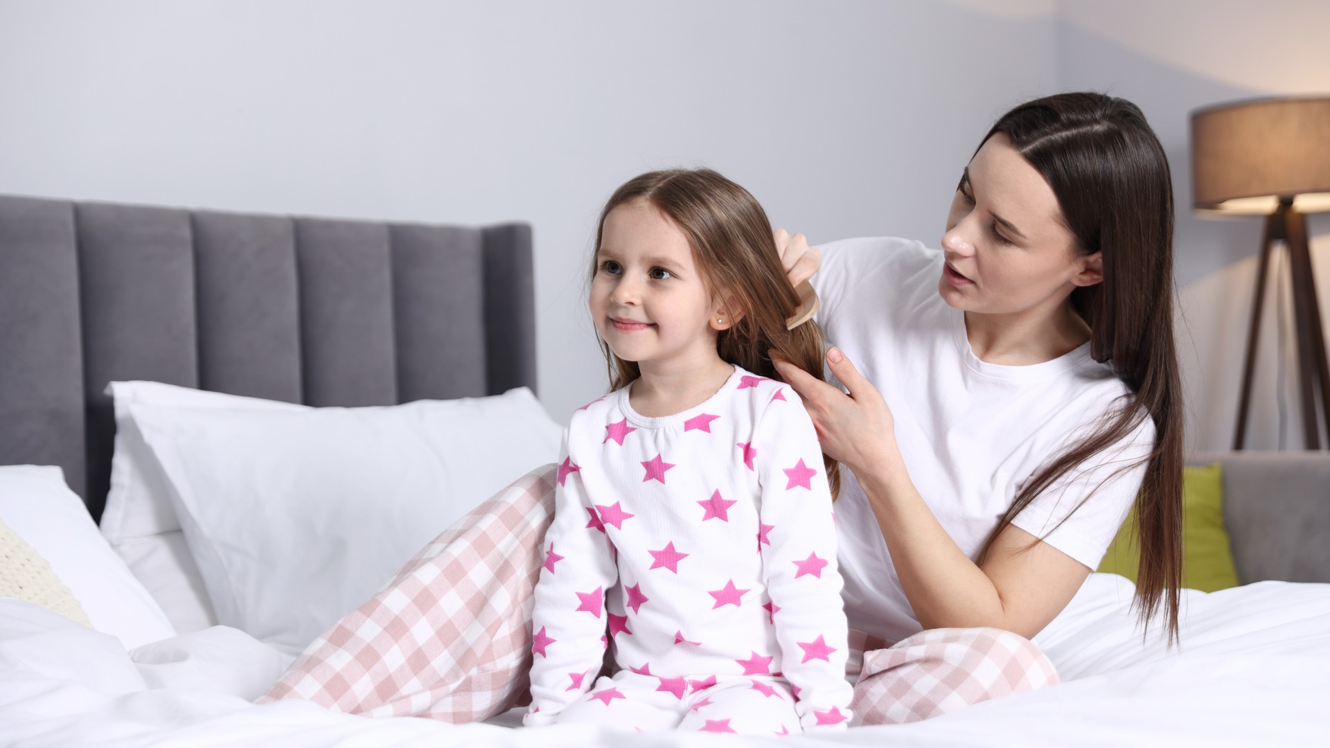 Parent gently combing through a child's hair on a bed at home, illustrating the calm head-check moment after spotting lice during a routine grooming session.