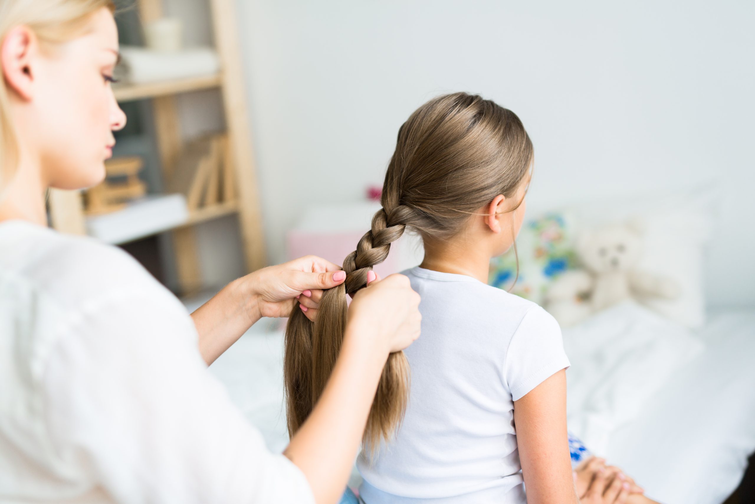 Parent braiding a child long hair into a protective hairstyle