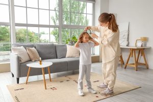 Mother using a handheld magnifying glass to check her young daughter's hair at home for head lice, framing the central identification decision moment of an at-home head check when a parent has spotted a tiny speck and is trying to tell whether it is a real head louse or one of the many look-alike bugs and debris that get mistaken for lice