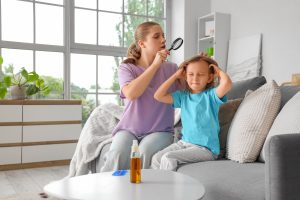 Mother using a handheld magnifying glass to inspect her young daughter's scalp at home, framing the article's actionable advice that the right reason to screen a child for head lice is a real human risk factor (school notification, sibling case, persistent scalp itching), not the discovery of chicken lice on backyard hens