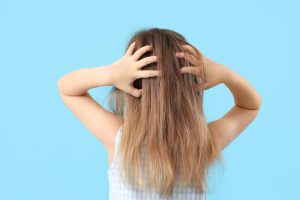 Back view of a young child scratching her irritated scalp on a plain background, framing the trigger scene the article opens on: a parent watching a child scratch for the third or fourth day and reaching for a pantry-based baking soda paste hoping it will calm the itch and end the head-lice case at the same time