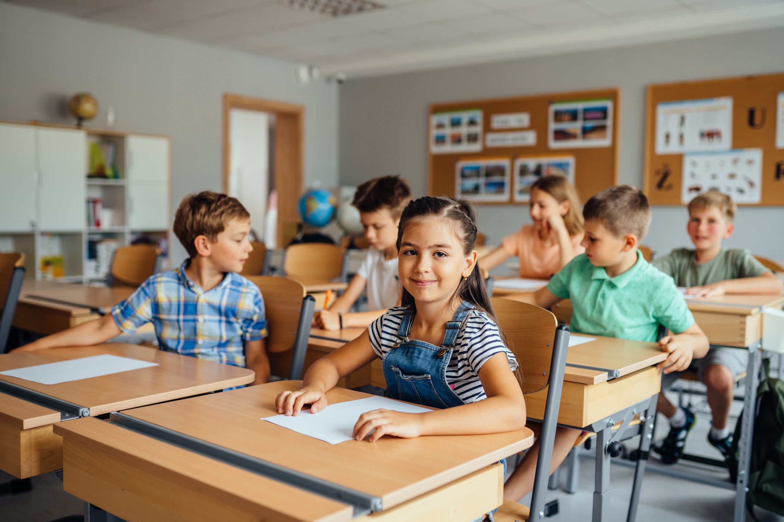 A diverse group of elementary students at their desks during a classroom lesson, illustrating where head lice spread through close contact at school.