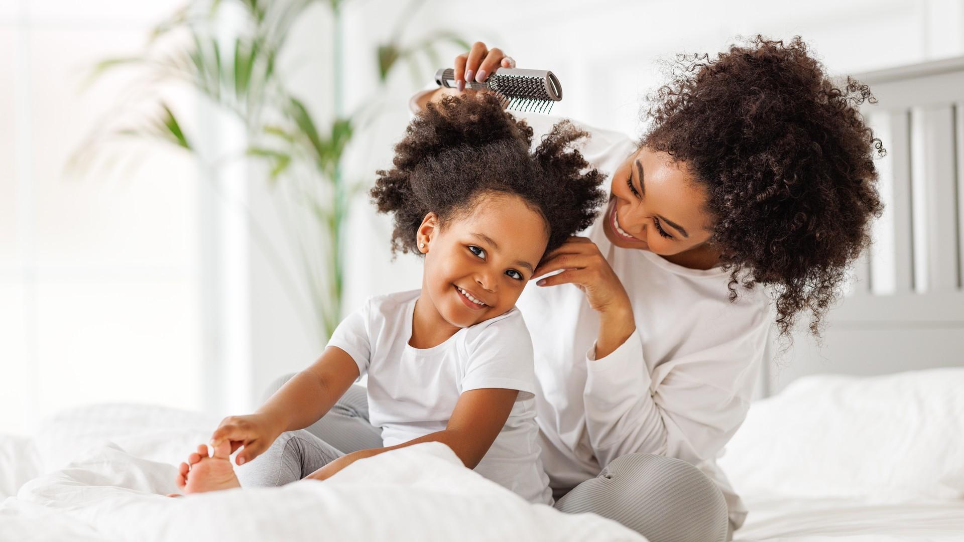 Mother brushing a child's long, thick, curly hair before a careful head lice check