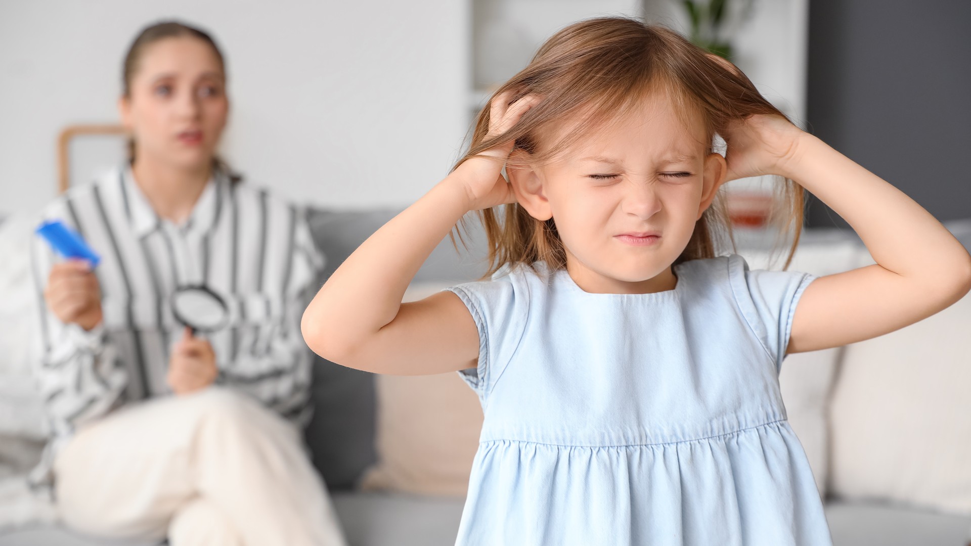 Child scratching her scalp while an adult prepares to check for untreated head lice