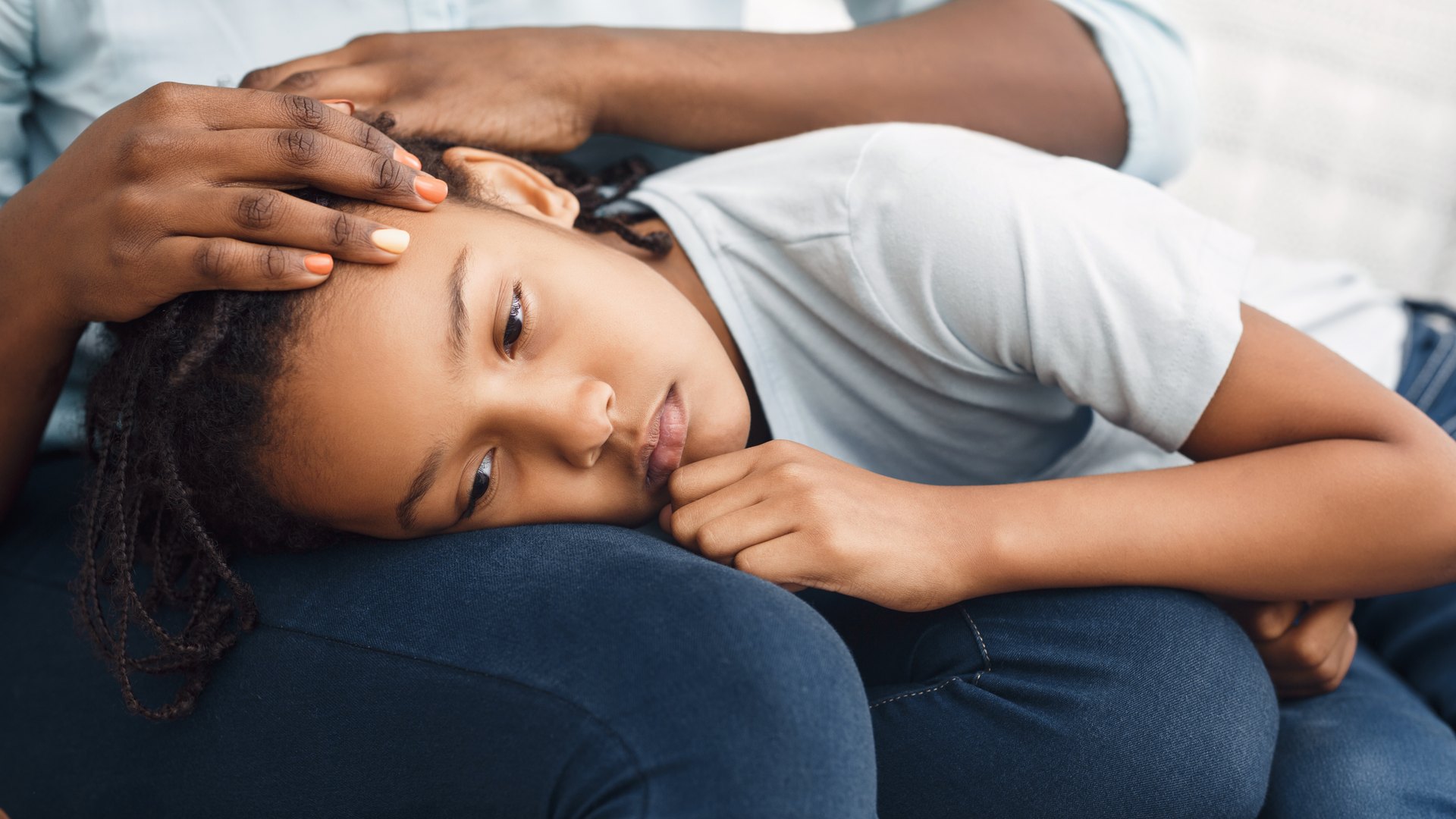 Child with locked hair resting head on a parent's lap while an adult hand holds the scalp
