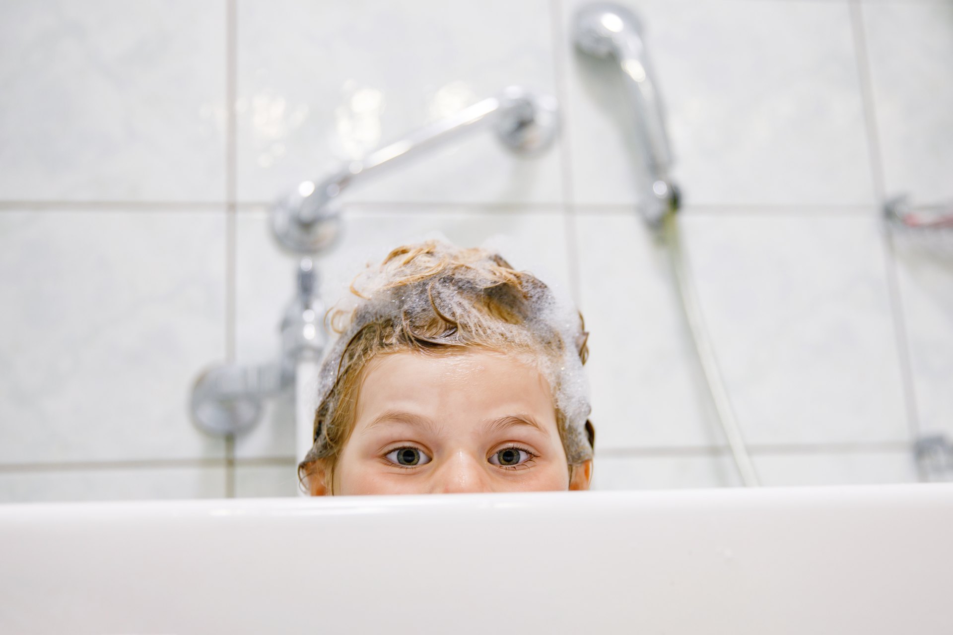 Child in a bath with soap foam covering their hair