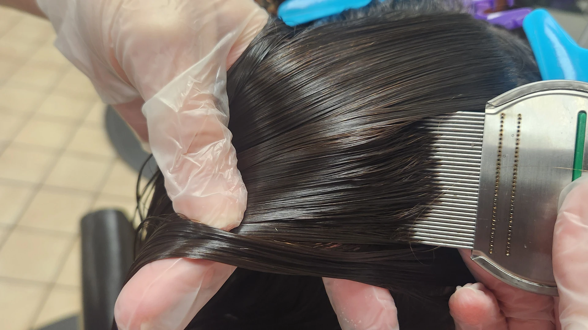 Gloved hands drawing a fine-tooth comb through a section of dark hair.